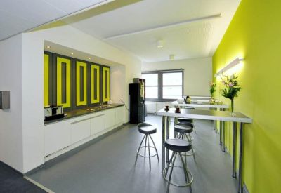 Bright communal kitchen and breakout area with a vibrant lime green feature wall and high stools.