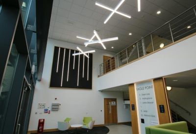 Double-height reception lobby with geometric pendant lighting and green accent chairs.