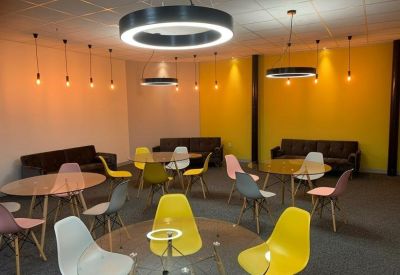Bright communal lounge with colorful seating, glass tables, and stylish ring pendant lighting.