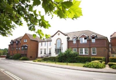 Wide view of the building exterior behind lush green trees and hedges.
