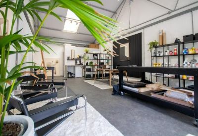 Bright open-plan studio with pitched roof, indoor plants, and black work tables.