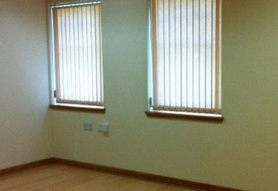 Empty room with wooden floors and two windows with vertical blinds.