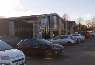 Modern stone-clad building facade with large glass windows and a front parking lot.