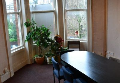 Bright boardroom with a dark oval table, blue chairs, and large bay windows.