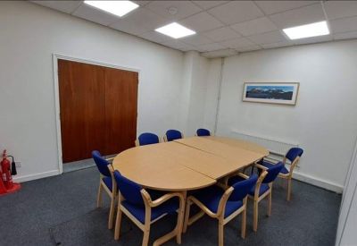 Professional meeting room with a large oval wooden table, blue chairs, and a framed landscape picture.