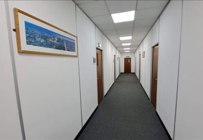 Bright, white office corridor with grey carpet and framed artwork on the wall.