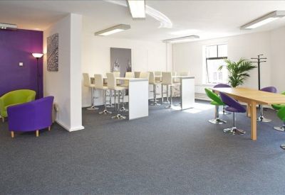 Spacious communal breakout area with white high tables and colorful chairs.