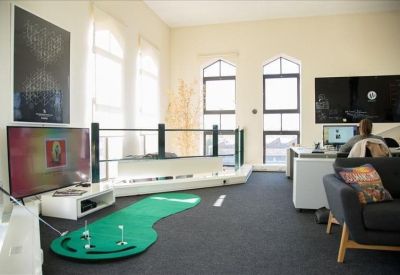 Modern lounge area with a putting green, flat-screen TV, and arched windows.