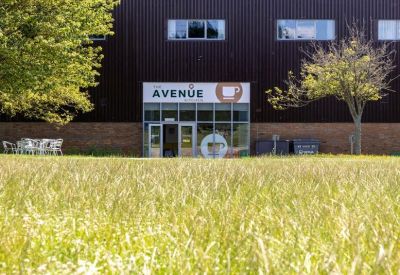 Outdoor seating area in front of The Avenue café with a green lawn in the foreground.