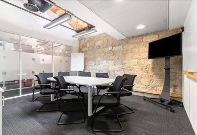 Bright meeting room with a large white table, stone walls, and a wall-mounted TV.