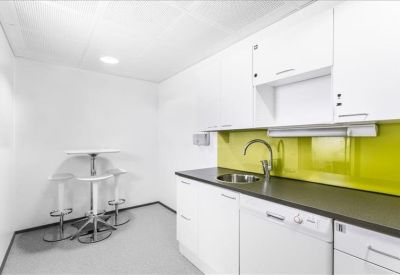 Modern office kitchen with white cabinetry, dark counters, and a lime green backsplash.