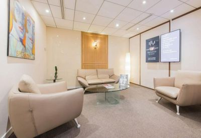 Bright waiting lounge with cream armchairs, a glass coffee table, and abstract wall art.
