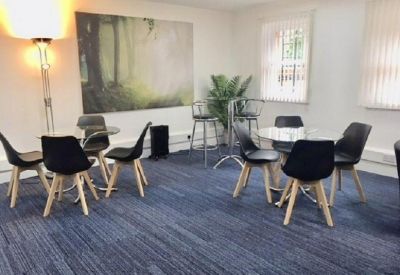 Bright breakout space with black chairs, round glass tables, and a large forest wall mural.