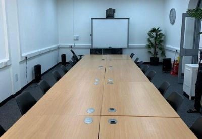 Long wooden boardroom table in a bright meeting room with a whiteboard and projector.