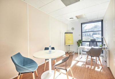 Private office featuring a circular meeting table, blue accent chair, and large window with natural light.