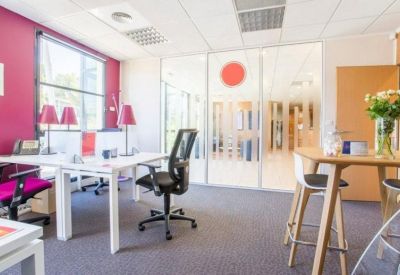 Bright workspace with a pink feature wall, white desks, and a wooden communal table with plants.