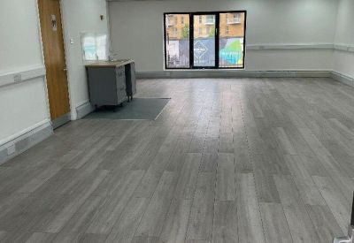 Spacious open-plan office with grey wood-effect flooring and a small kitchenette.