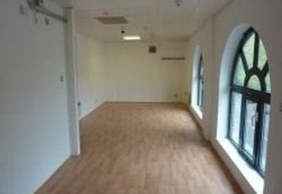 Long office space with wood-style flooring and large arched windows.