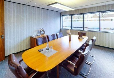Professional boardroom with a long oval wood table, leather chairs, and large windows.