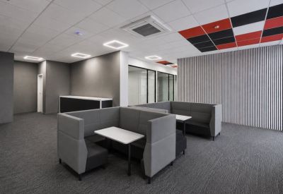 Communal breakout area with grey upholstered high-back booths and white tables.