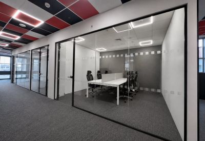 Modern glass-walled private office suite with white desks and black ergonomic chairs.