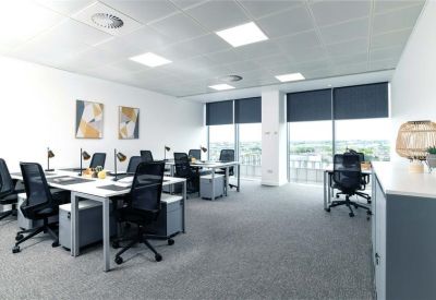 Sunlit open-plan office with white desks, mesh chairs, and large windows.