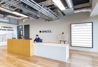 Sleek reception area with a wood and white front desk and 'Spaces' branding.