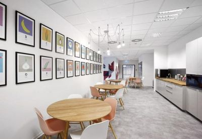 Spacious communal kitchen and dining area with round wooden tables, colorful chairs, and fruit-themed wall art.