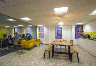 Spacious communal breakout area with yellow sofas, wooden dining table, and a modern kitchen unit.