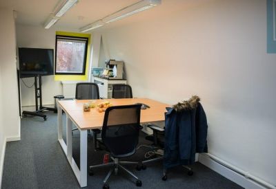 Small meeting room with a central wooden table, black chairs, and a large wall-mounted monitor.