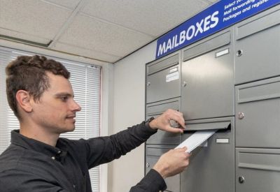 Close-up of a person accessing a wall of grey metal mailboxes in a lobby area.