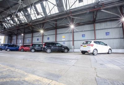 Spacious indoor parking area with several cars parked under a high industrial ceiling.