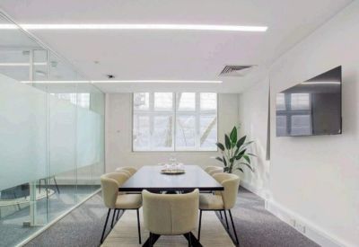 Minimalist meeting room with a dark wood table, cream chairs, and a wall-mounted TV screen.
