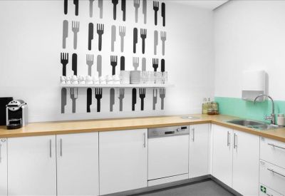 Modern office kitchen with white cabinetry, light wood countertops, and a fork and knife wall mural.