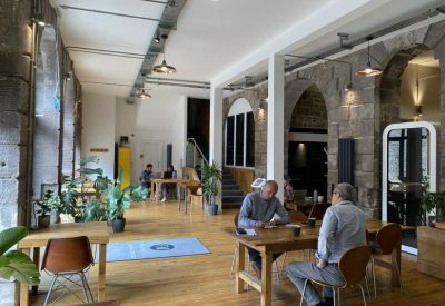 Spacious communal lounge with arched stone walls, wooden floors, and potted plants.