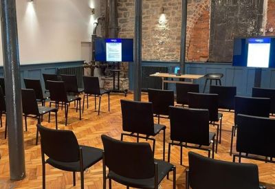 Modern presentation room with black chairs and dual display screens against a stone wall.