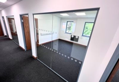 Bright hallway showing private glass-fronted offices with dark carpeting.