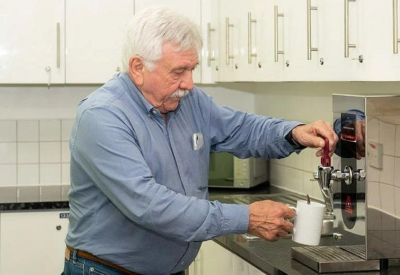 An employee using a water dispenser in a clean white office kitchenette.