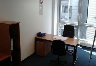 Private office featuring a wooden desk, two black chairs, and a large window with natural light.