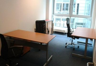 Bright workspace with two separate desks and black ergonomic chairs near a large window.