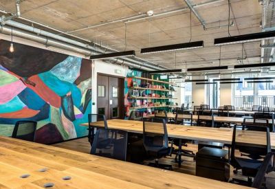 Open-plan office with rows of wooden desks and industrial exposed ceilings.