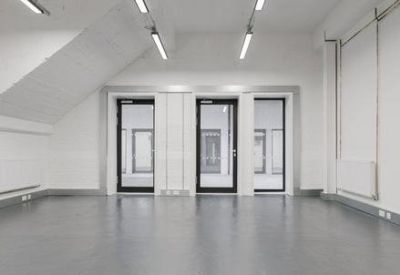 Large empty open-plan office space with white walls and industrial lighting.