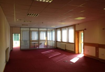 Spacious open-plan office area with red carpeting and glass partitions under a grid ceiling.