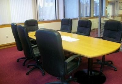 Conference room featuring a large light wood table and eight black leather executive chairs.