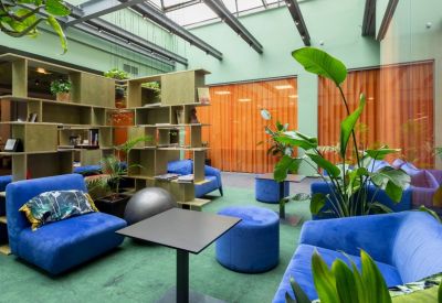 Sunlit lounge area with blue velvet seating, green carpet, and a glass ceiling.