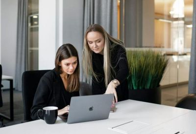 Two women collaborating over a laptop in a modern office setting.