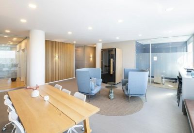 Bright breakout area with high-back blue armchairs and a wooden communal table.