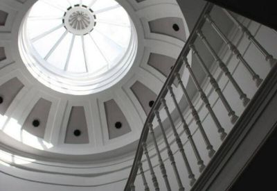A dramatic interior view looking up at a white circular skylight and elegant curved staircase.
