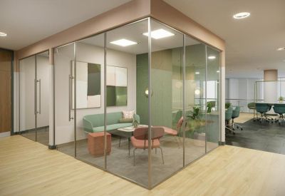 Glass-walled private meeting room with soft green walls, a grey sofa, and pink accent chairs.