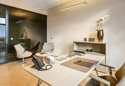 Private office suite featuring a white desk, grey armchairs, and a glass partition wall.